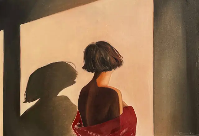 Woman with a bob haircut facing a lit wall, her shadow beside her, red cloth at her shoulders
